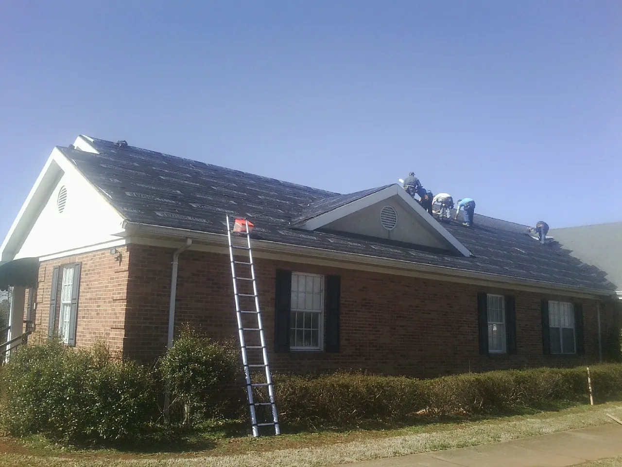 Crew tearing shingles off a brick ranch roof with a ladder set — Emergency Roof Repair work by our crew in Abell