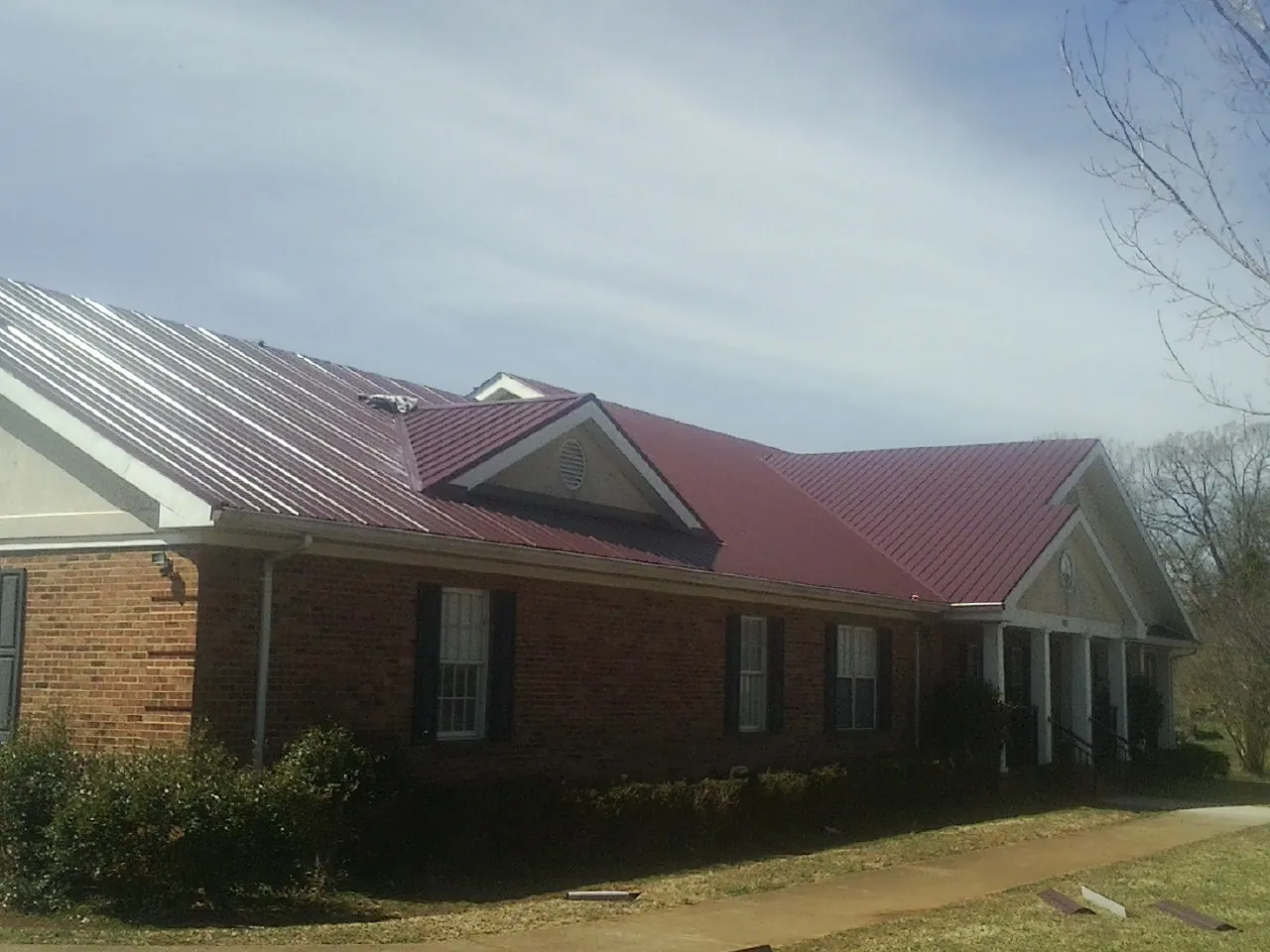 Red metal roof with gabled entries on a long brick building, from a Hail Damage Roof Repair job in Abell
