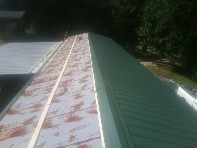 Old rusted panels beside newly installed green metal roofing — Wind Damage Roof Repair by Roofing Brothers in Abell