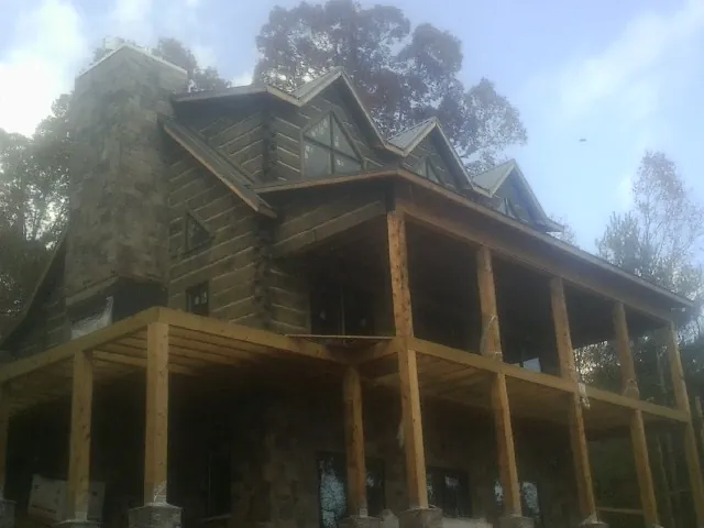 Stone chimney and dormers on a large log home with a timber porch in Abell