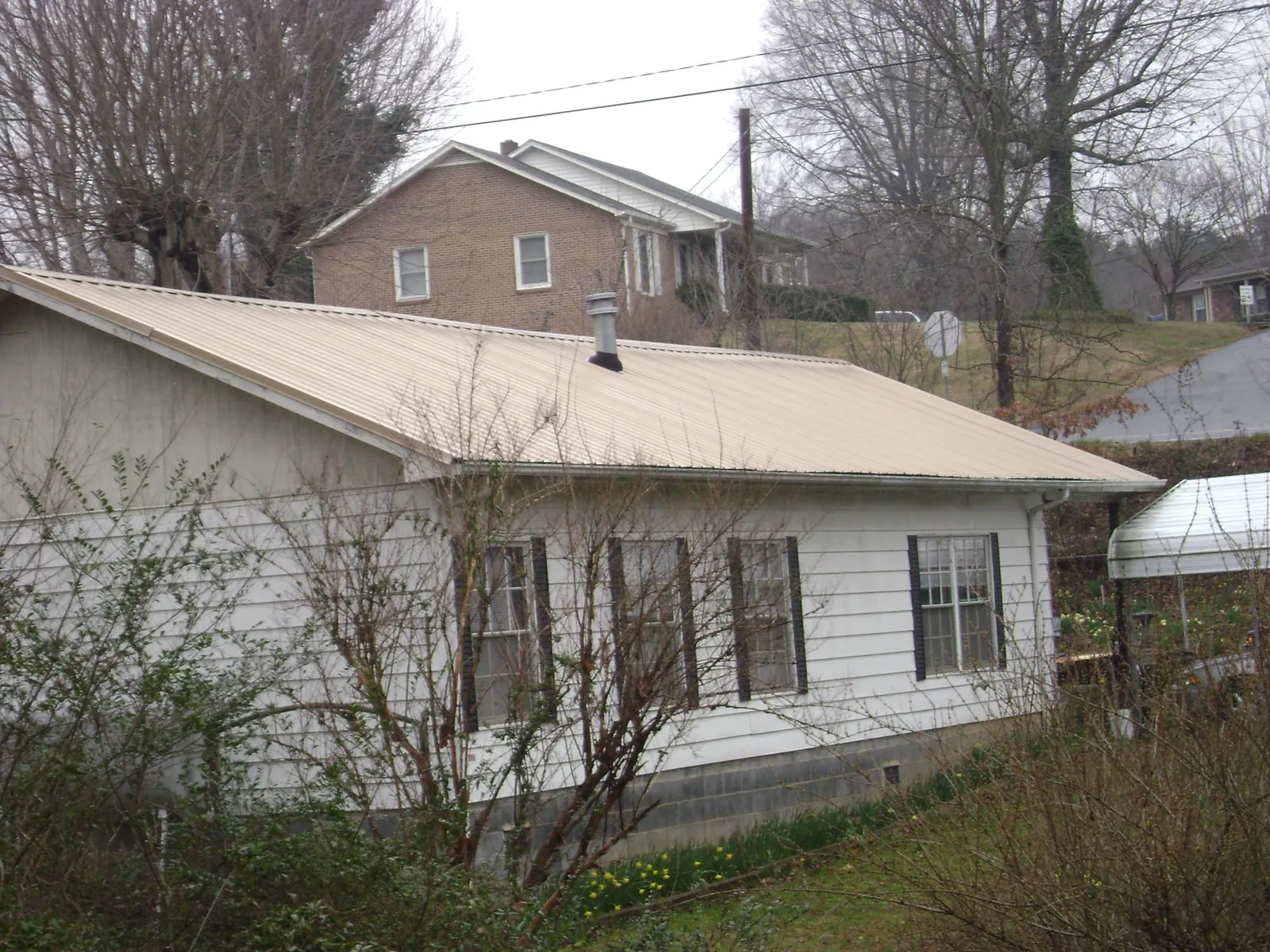 Tan metal roof on a white sided house set into a hillside — Commercial Roofing by Roofing Brothers in Abell