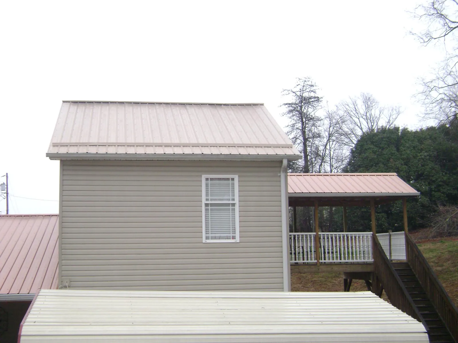 Tan metal roofs on a two story addition and attached porch, from a Roof Replacement job in Abell